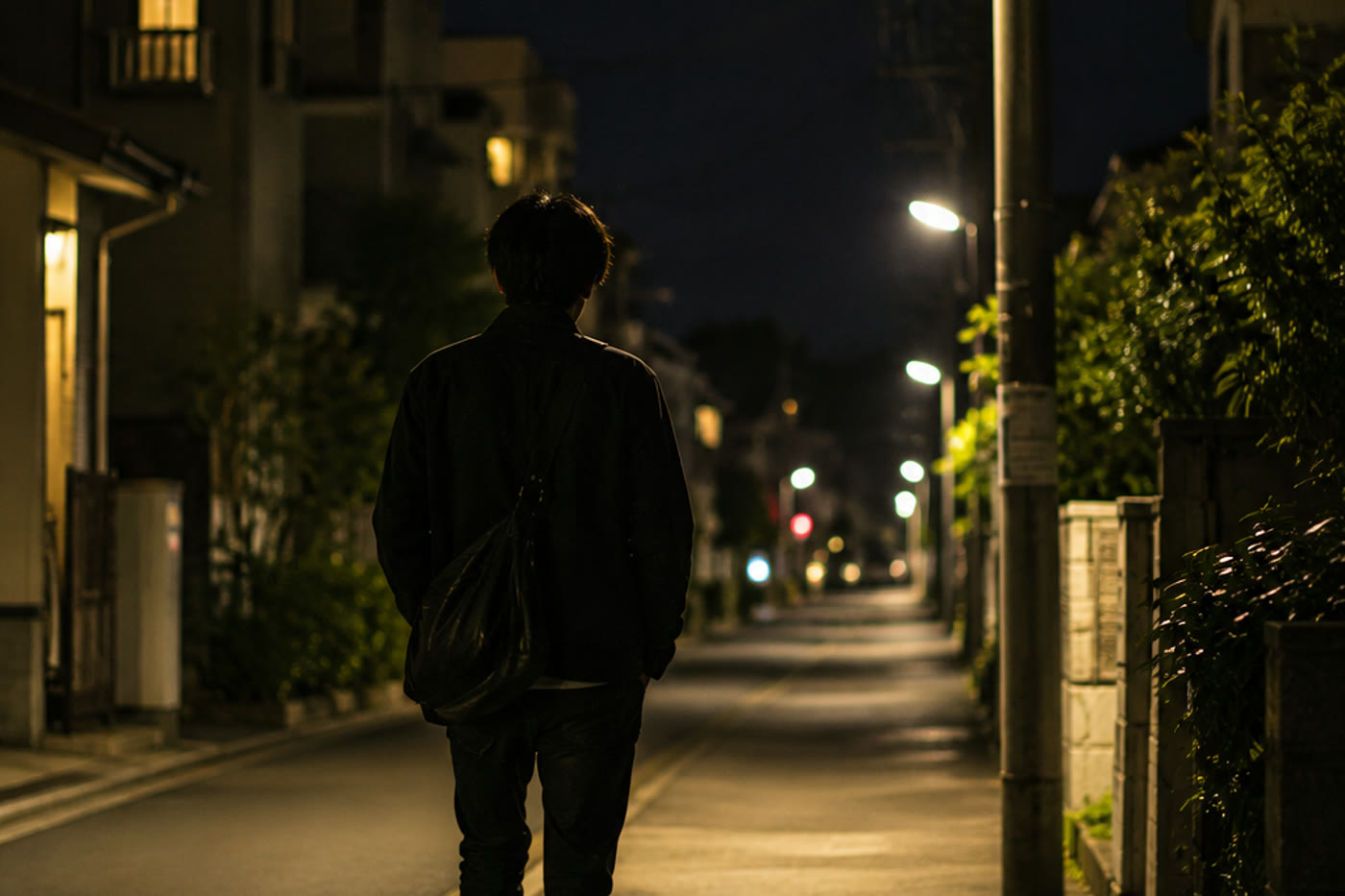 夜の住宅街をひとりで歩いて帰る人の後ろ姿